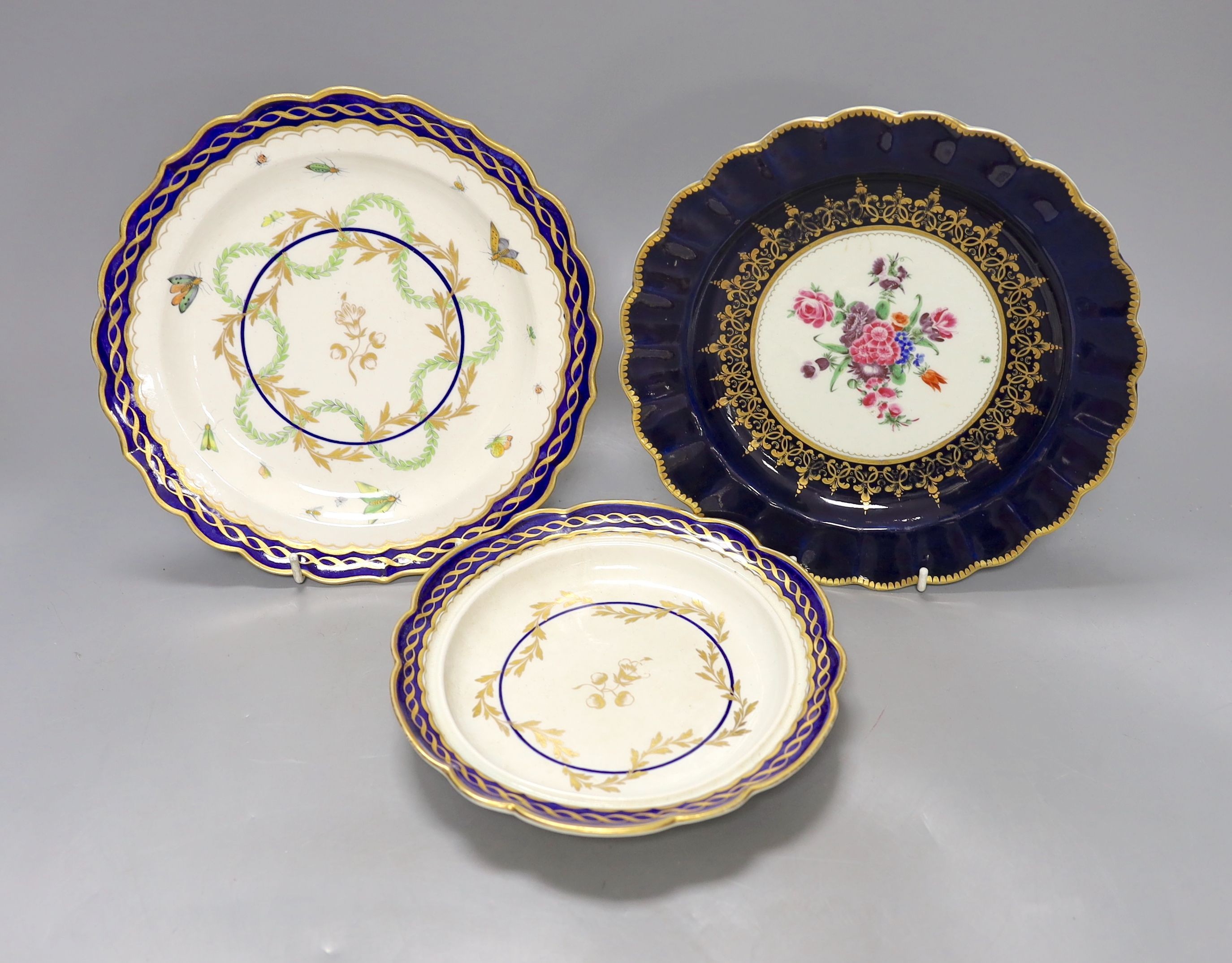 Three Worcester plates having blue border, one with elaborated gilding enclosing a bouquet of flowers, two plates both with a star shaped foliate design in the centre, c.1775, largest 21.5 cm